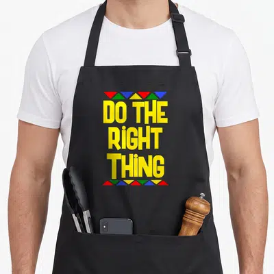 Tablier de cuisine noir avec inscription jaune Do The Right Thing encadrée de triangles rouges verts bleus et jaunes.