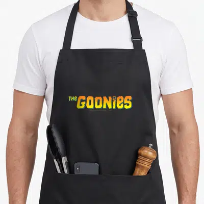 Tablier de cuisine noir avec le logo The Goonies en lettres jaunes et oranges style vintage