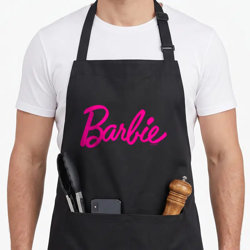 Tablier de cuisine noir avec le logo Barbie écrit en rose vif au centre.