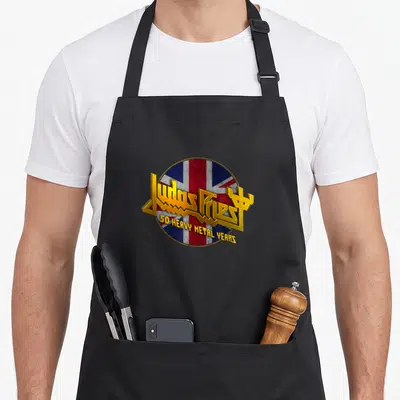 Tablier de cuisine noir avec logo Judas Priest 50 Heavy Metal Years sur fond Union Jack circulaire aux couleurs vives et effet métallique doré.