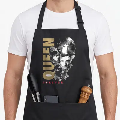 Tablier de cuisine noir avec le texte Queen en doré et des portraits artistiques en noir et blanc sur le devant.