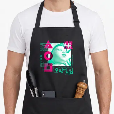 Tablier de cuisine noir avec une illustration graphique rose et turquoise représentant une poupée et des symboles géométriques.