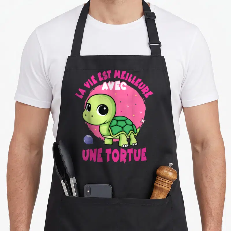 Tablier de cuisine noir avec une tortue verte et le texte la vie est meilleure avec une tortue sur fond rose.