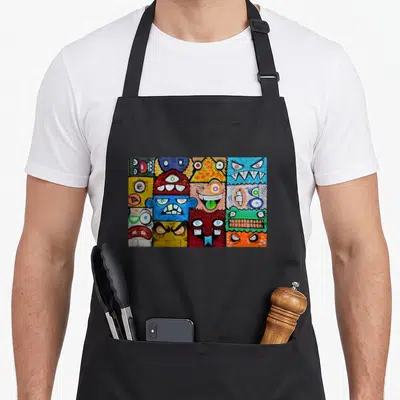 Tablier de cuisine noir orné d'une illustration murale de monstres graffiti multicolores aux yeux multiples et sourires édentés.