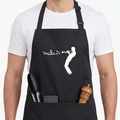 Tablier de cuisine noir avec silhouette blanche d'un musicien jouant du trompette et l'inscription miles en écriture cursive à côté.