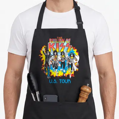 Tablier de cuisine noir avec illustration de quatre musiciens en maquillage de scène entourés de flammes jaunes et bleues sous le texte The Return of Kiss U.S. Tour.