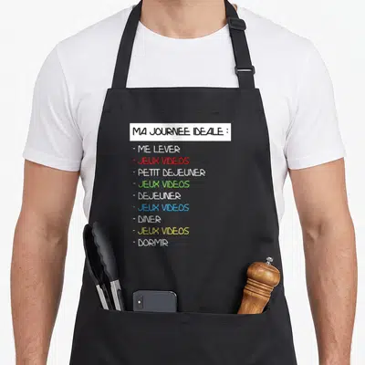 Tablier de cuisine noir avec liste imprimée Ma journée idéale alternant repas et jeux vidéos en couleurs vives sur fond blanc.