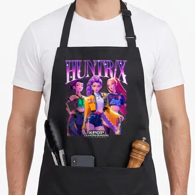 Tablier de cuisine noir avec l'illustration des trois membres du groupe Huntrix et leur nom en lettres violettes scintillantes.