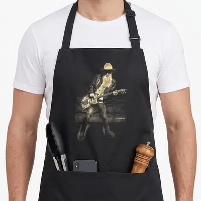 Tablier de cuisine noir avec illustration dorée d'un guitariste au chapeau jouant devant des amplificateurs.