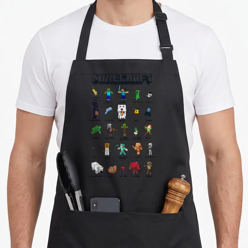 Tablier de cuisine noir avec un collage coloré de personnages pixelisés Minecraft et leurs noms en dessous.