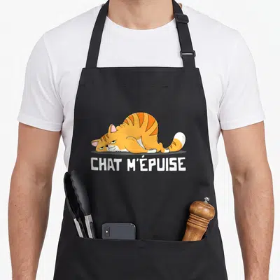 Tablier de cuisine noir avec illustration d'un chat tigré orange allongé et du texte blanc CHAT M'ÉPUISE en dessous.