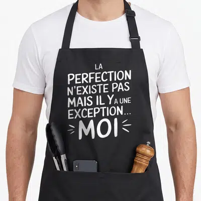 Tablier de cuisine noir avec le texte blanc La perfection n'existe pas mais il y a une exception moi accentué par des traits graphiques.