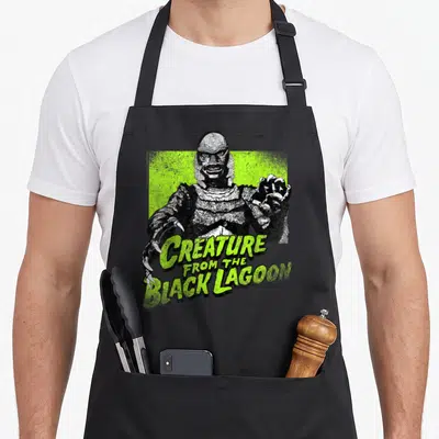 Tablier de cuisine noir avec illustration verte du monstre aquatique aux griffes acérées et texte stylisé.