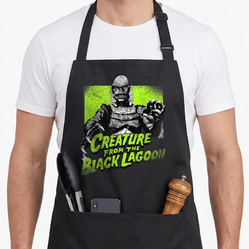 Tablier de cuisine noir avec illustration verte du monstre aquatique aux griffes acérées et texte stylisé.