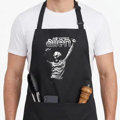 Tablier de cuisine noir avec illustration blanche d'un alien aux bras levés et le texte alien resident en haut.
