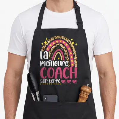 Tablier de cuisine noir avec arc-en-ciel léopard et texte La meilleure coach sur terre en rose et blanc.