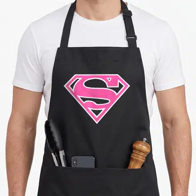 Tablier de cuisine noir avec le logo S de Supergirl en rose vif et contour blanc au centre.
