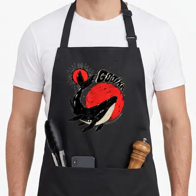 Tablier de cuisine noir avec illustration d'une baleine noire nommée Gojira devant un soleil rouge stylisé et des étoiles.