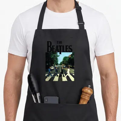 Tablier de cuisine noir avec les Beatles traversant Abbey Road sous leur nom imprimé en lettres noires.