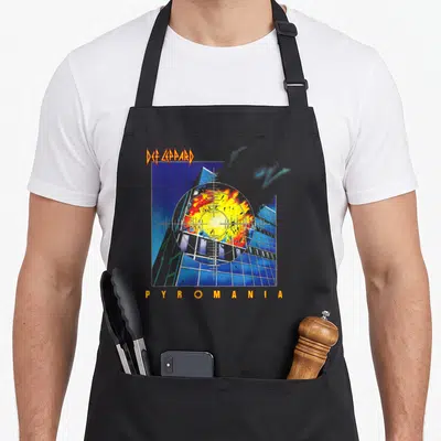 Tablier de cuisine noir avec une illustration d'explosion dans un viseur sur fond bleu et des textes oranges.