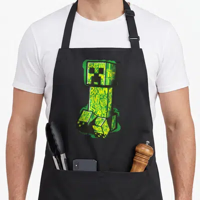 Tablier de cuisine noir avec illustration Creeper Minecraft en graffiti vert et jaune portant les mots Boom et TNT.