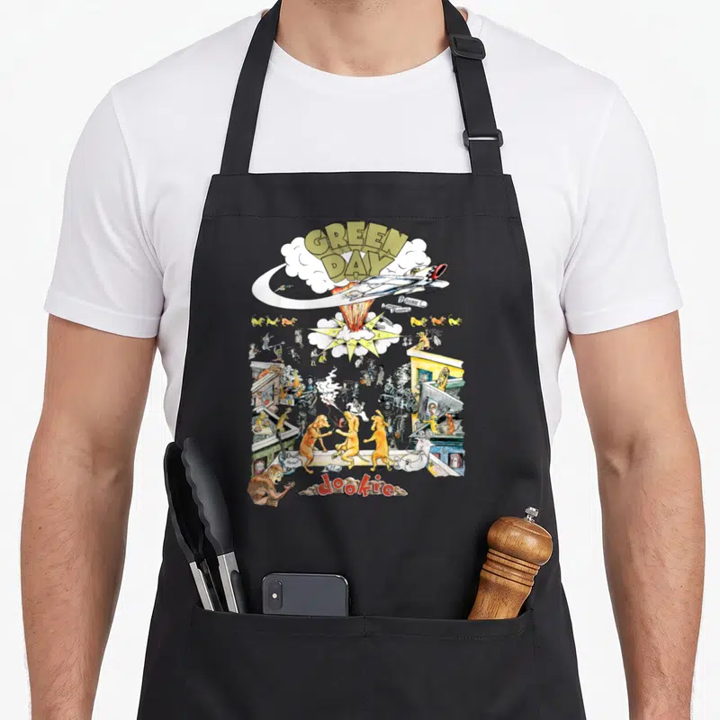 Tablier de cuisine noir avec illustration colorée d'un avion s'écrasant sur une rue animée de chiens et de personnages.