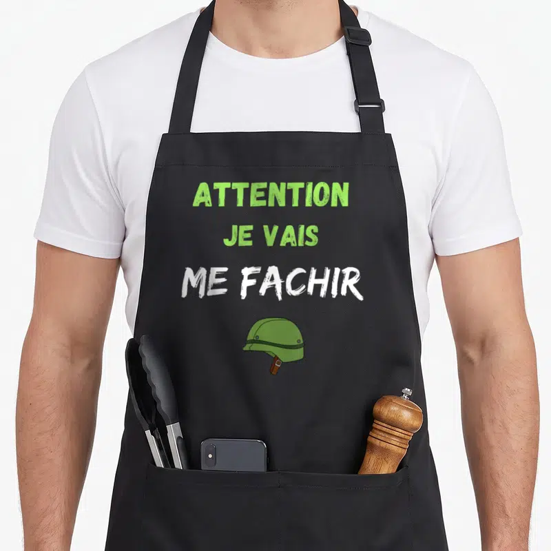 Tablier de cuisine noir avec texte Attention je vais me fachir et illustration de casque militaire vert en dessous.