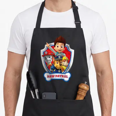 Tablier de cuisine noir avec illustration colorée du badge Paw Patrol et des personnages animés.