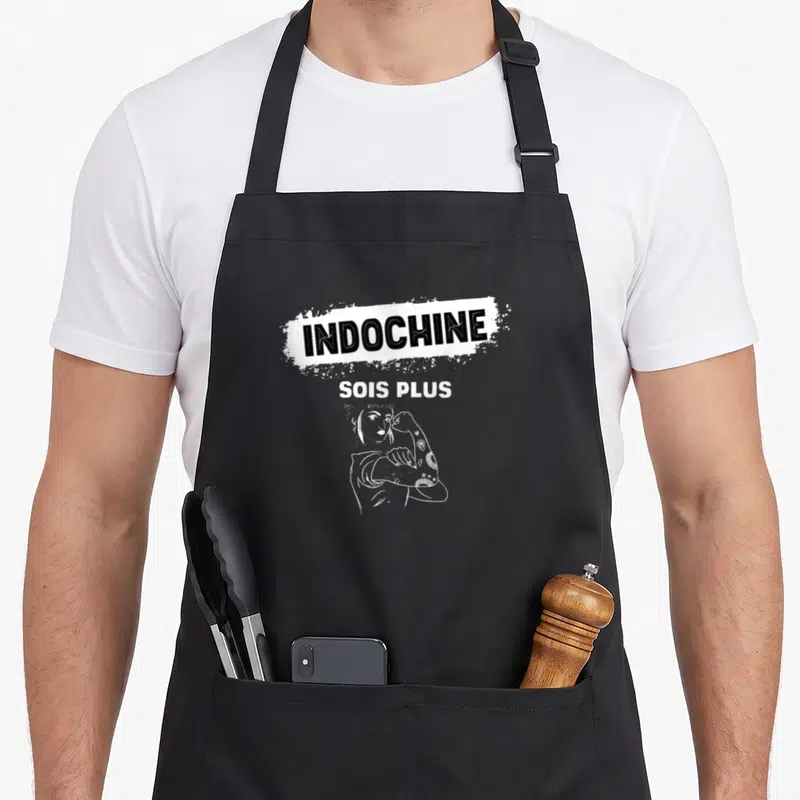 Tablier de cuisine noir avec inscription Indochine Sois Plus Fort et dessin femme tatouée en blanc.