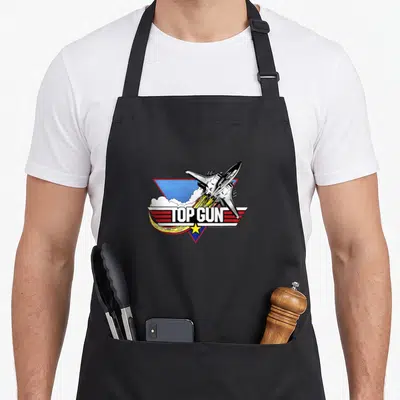 Tablier de cuisine noir avec un avion de chasse, des ailes rouges et le texte Top Gun au centre.