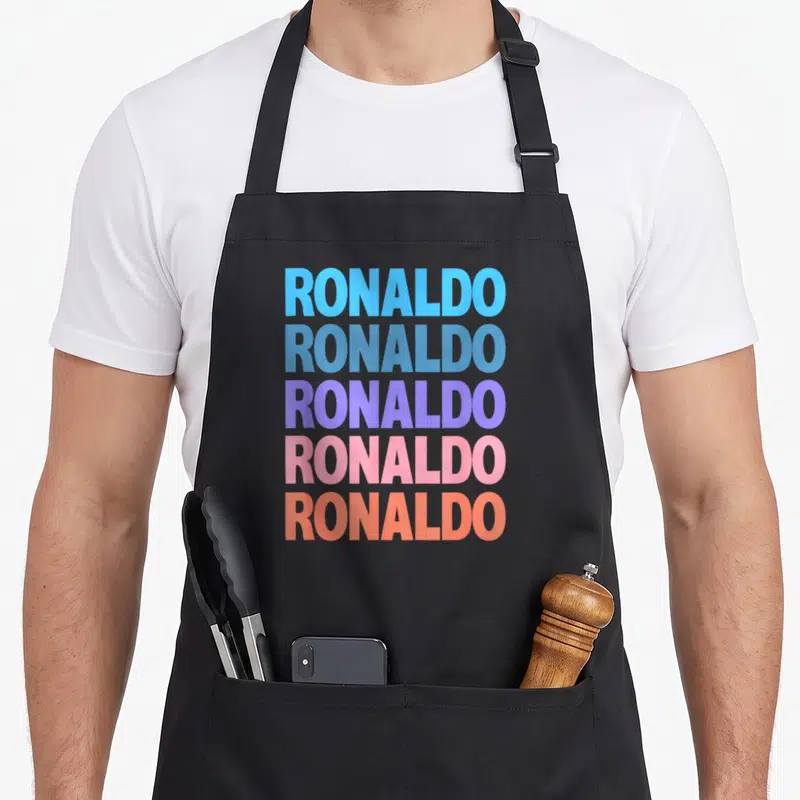 Tablier de cuisine noir avec le texte RONALDO répété en lettres majuscules aux couleurs dégradées.