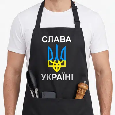 Tablier de cuisine noir avec le trident ukrainien bleu et jaune encadré par les mots en blanc.