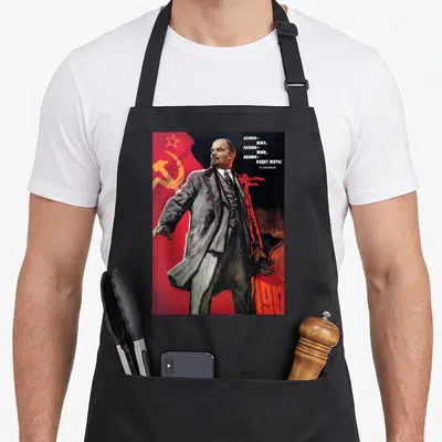 Tablier de cuisine noir avec illustration de Lénine sur fond de drapeau rouge soviétique et texte en russe.