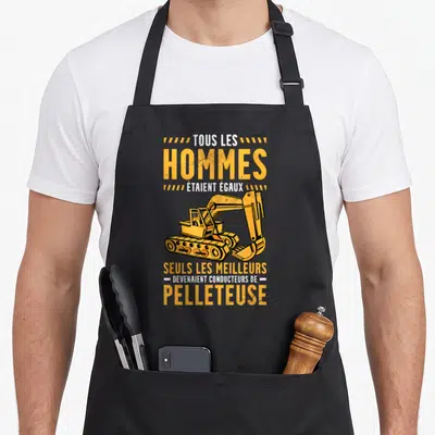 Tablier de cuisine noir avec une pelleteuse jaune et le texte tous les hommes étaient égaux seuls les meilleurs devenaient conducteurs de pelleteuse