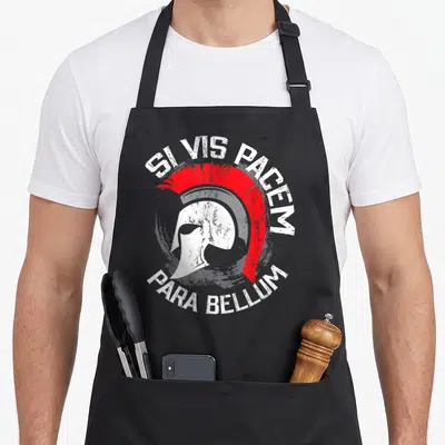 Tablier de cuisine noir avec illustration casque spartate rouge et texte latin Si Vis Pacem Para Bellum en cercle.