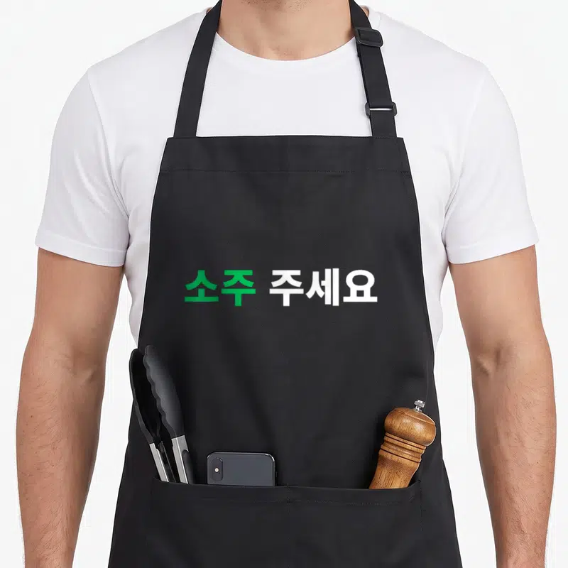 Tablier de cuisine noir avec le texte en hangul en vert et blanc au centre.