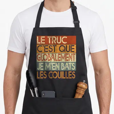 Tablier de cuisine noir avec inscription Le Truc C'est Que Globalement Je M'en Bats Les Couilles sur fond de bandes colorées vintage.
