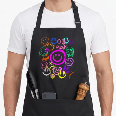 Tablier de cuisine noir avec smileys graffitis multicolores, émoticônes vives et effets de peinture qui dégouline.