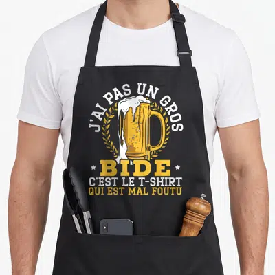 Tablier de cuisine noir avec illustration de grande bière déversée entourée de texte humoristique blanc et jaune.