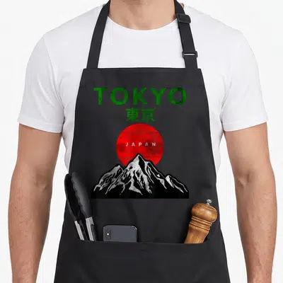 Tablier de cuisine noir avec l'inscription TOKYO, un soleil rouge et une montagne stylisée en noir et blanc.