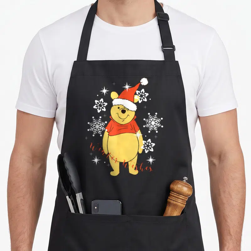 Tablier de cuisine noir avec Winnie l'ourson en bonnet de Noël et flocons blancs.