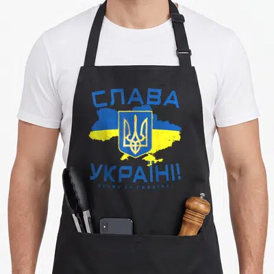 Tablier de cuisine noir avec Slava Ukraini en cyrillique, le Tryzub central et une carte aux couleurs bleue et jaune.