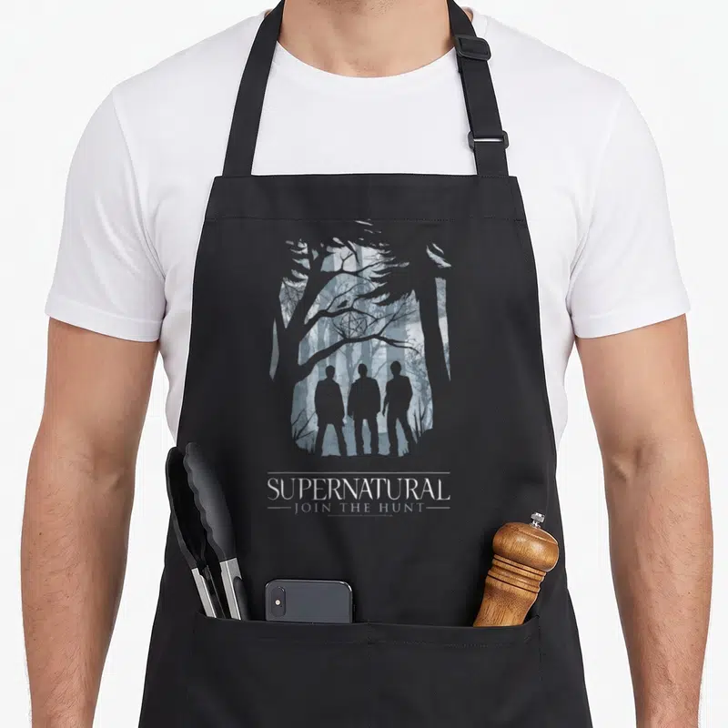 Tablier de cuisine noir avec trois silhouettes humaines devant des arbres et le texte supernatural join the hunt.