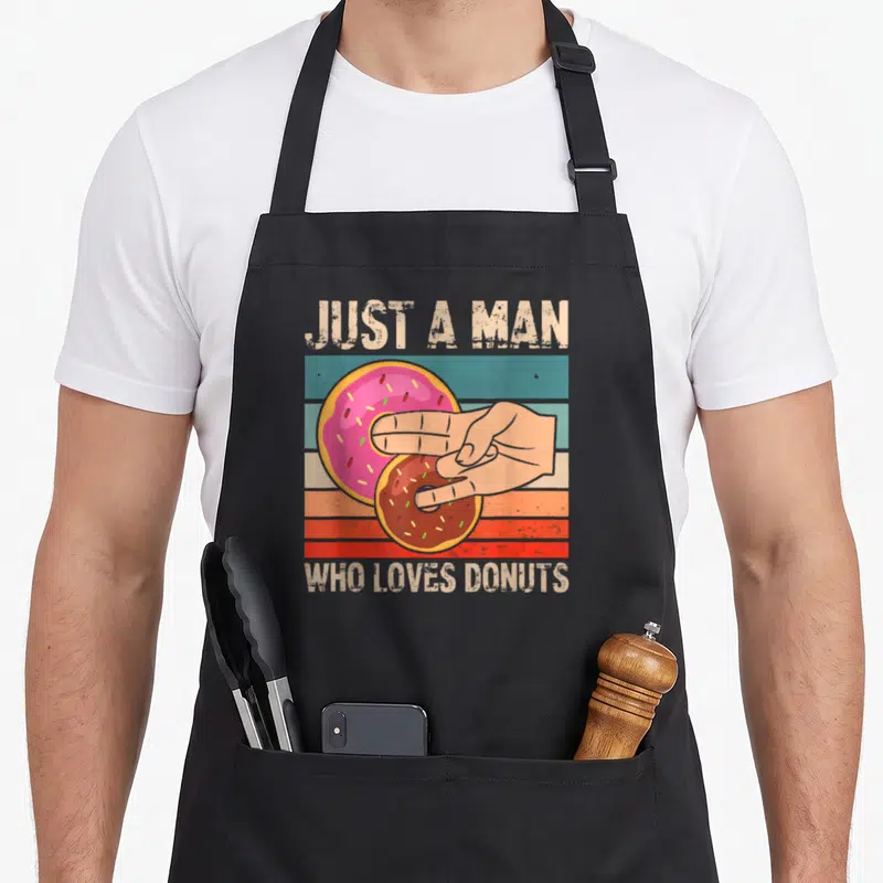 Tablier de cuisine noir avec illustration vintage d'une main tenant un beignet rose et un beignet chocolat sur fond de bandes colorées.