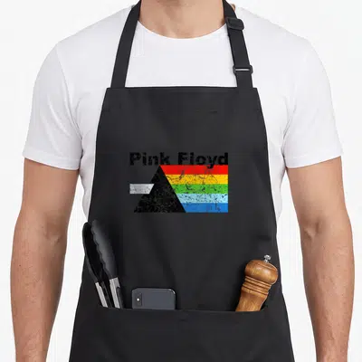 Tablier de cuisine noir avec le texte Pink Floyd au-dessus d'un prisme dispersant un arc-en-ciel aux couleurs vives et texturées.