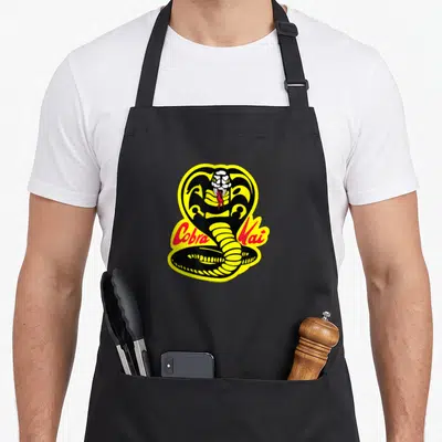 Tablier de cuisine noir avec illustration d'un cobra jaune et noir portant l'inscription Cobra Kai en lettres rouges stylisées.