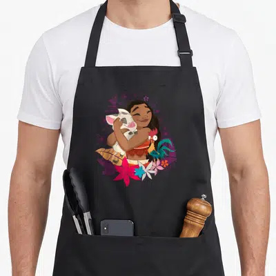 Tablier de cuisine noir avec Vaiana, Pua et Hei Hei entourés de fleurs tropicales et motifs polynésiens violets.