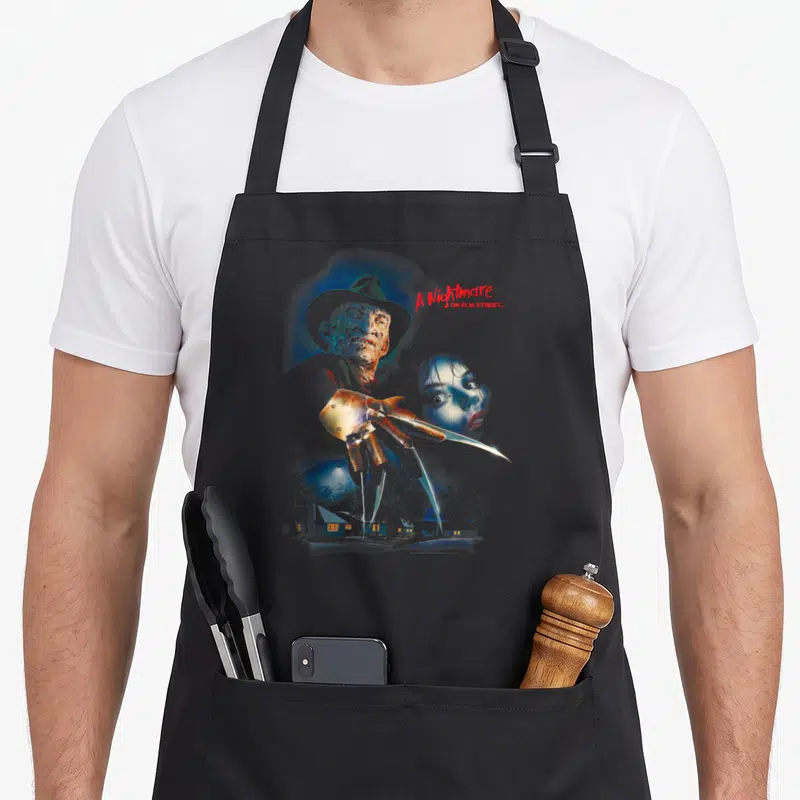 Tablier de cuisine noir avec illustration de Freddy Krueger, sa gantade à lames et le titre A Nightmare on Elm Street en rouge.
