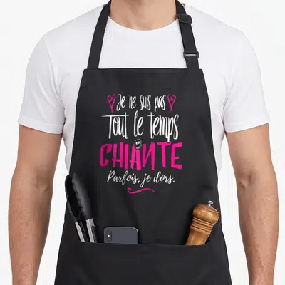 Tablier de cuisine noir avec une citation humoristique en blanc et rose vif sur fond uni.