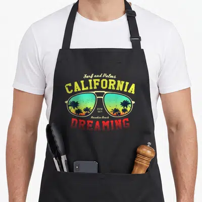Tablier de cuisine noir avec un motif rétro affichant des lunettes de soleil et des palmiers au coucher du soleil.